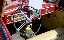 Palubní deska Škody 1101 se sdruženým panelem, tříramenným volantem a řadicí pákou na podlaze. Uprostřed mřížka autorádia, pod volantem táhlo ruční brzdy.