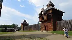 Barevná současná fotografie; v centru a vpravo palisáda dvojnásobné výše člověka uprostřed s dřevěnou patrovou věží s věžičkou. Na pozadí vlevo přízemní dřevěné domky.