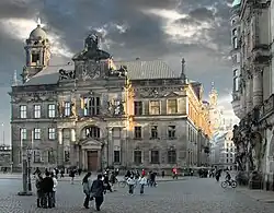 Barevná fotografie s pohledem na vrcholně barokní palác s průčelím a věží, za nímž je vidět kostel Frauenkirche