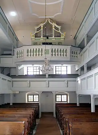 Interiér kostela, dole dřevěné lavice, vpředu a po pravé straně světlé dvoupatrové empory, uprostřed v horní části stojí varhany.