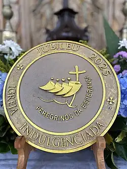 Logo Svatého roku 2025 Obsahuje čtyři stylizované postavy, které se vzájemně objímají; první z nich je kříž držený v podobě kříže nad rozbouřenými vlnami. Kříž se táhne až ke dnu v podobě kotvy.[1]