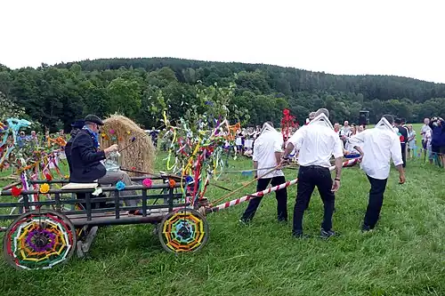Průvod v čele s Pazderníkem a kecalem přijeli k boudě Konopičky; žebřiňák táhnou 4 koně – místní mládenci