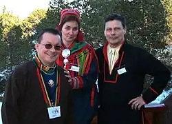 Dva stojící muži a uprostřed stojící žena v tradičních sámských oblecích