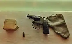 Revolver, ležící vedle prázdného pouzdra, krabička s náboji a osamocený náboj