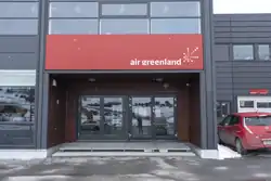 Sídlo Air Greenland v Nuuku. Je zachycen hlavně vstup, nad kterým se nachází červené cedule s názvem společnosti. Celá budova je prosklená a má tmavě šedou konstrukci.