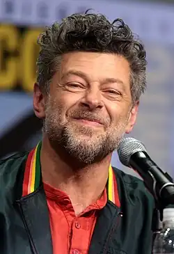 Usmívající se herec Andy Serkis sedí na židli na pódiu na comic conu