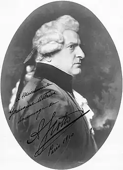 Pravý profil přísně stojícího muže v tmavém oblečení s krajkovými manžetami a košili, má paruku