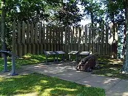 Wooden posts in a semicircle around information boards and a cannon