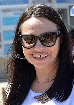 Smějící se černovlasá žena se slunečními brýlemi.