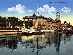 Socha Borussia (dnes je na stejném místě socha rybáře) v Klaipėdě. Pohled přes řeku Danė. Budovy na fotografii (s vyšší věžičkou – pošta, s nižší – Burza) již neexistují, byly zničeny koncem II. svět. války, trosky odklizeny po válce. Mezi dvěma největšími budovami vpravo je patrný okraj mostu Biržos tiltas (Burzovní most). Pohled k východoseverovýchodu