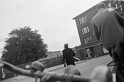 Menno Huizinga: Špionážní fotografie, dole v popředí jsou vidět řídítka Huizingova kola, žena dokázala koupit oranžovou vlajku, 1944–1945