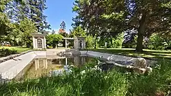 Bazén a dva altány spojené pergolou, v popředí kašna s hlavou lva