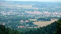 Barevná fotografie s pohledem na zalesněnou krajinu v jejímž středu se rozkládá město Žitava