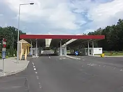 Asfaltová silnice vedoucí hraničním přechodem majícím podobu přízemních staveb s vodorovnou střechou zakrývající vozovku.