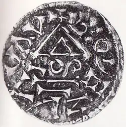 Černobílá fotografie. Mince pokrytá různými znaky a nečitelnými písmeny.