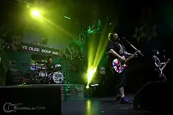 Obrázek z koncertu, bubeník Wiseman za bicími, frontman Reddick zpívá a hraje na svou texaskou kytaru, vedle něho baskytarista Chandler