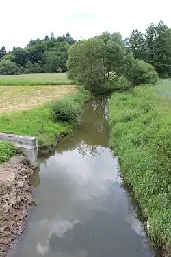 Koryto vodního toku, napravo louka, nalevo pole a betonové koryto, jímž přitéká potok od Bratronic.