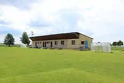 Přízemní zděná budova šaten a zázemí fotbalistů. Nalevo i napravo od budovy jsou samostatně stojící plastové přístřešky – lavičky soupeřících mužstev.