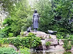 Čelní pohled na kašnu. Uprostřed je socha dívky s husami. Pod ní lze vidět vyvěrající vodu ze skály a část jezírka.