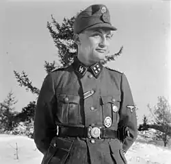Gunter d’Alquen jako SS-Sturmbannführer během roku 1941. Na jeho levé kapse můžeme vidět v horní části zlatý stranický odznak, pod ním všeobecný útočný odznak a v druhé horní knoflíkové dírce je stuha od železného kříže II. třídy.