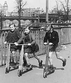 Pouliční scéna z Berlína r. 1948, děti s dřevěnou koloběžkou