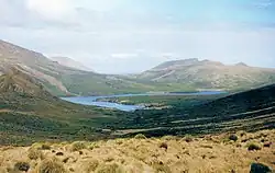 Fotografie údolí s jemně se svažujícími svahy porostlé travinami a křovisky. V délce je vidět záliv a nevelké kopce