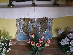 Kamenná deska z erbem opřená o zeď obklopená květinami v květináčích.