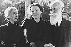 Na černobílé fotografii na šířku je Charlotte se svými prarodiči. Jako mladá dívka stojí mezi ženou s bílými vlasy a černých šatech, která se na ni dívá. Napravo stojí dědeček se světlými vousy hledící šikmo dolů.