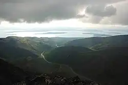 Pohled do zelenošedého údolí s prudkými srázy, vzadu rozsáhlá vodní plocha