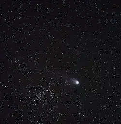 Fotografie komety, která na obloze zdánlivě prolétá kolem hvězdokupy Jesličky. Uprostřed snímku je jasná hvězda Asellus Borealis, hvězdokupa je vlevo dole a jádro komety vpravo dole.