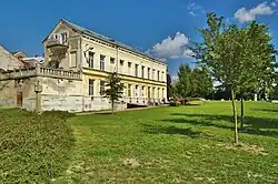 Pohled od muzea na vysokou dvoupodlažní budovu se žlutou fasádou ve Smyčkově ulici v Litovli. Vpředu k budově přiléhá nízká oprýskaná přístavba s terasou a kamenným zábradlím na střeše.