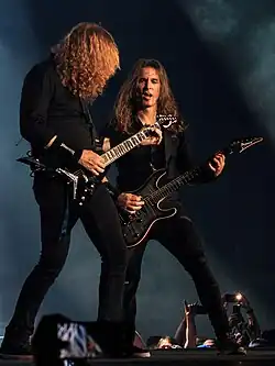 Dva dlouhovlasí kytaristé vystupující na pódiu