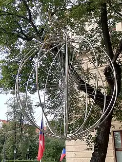 Detail visícího symbolického bicyklu s dívčí postavou na vrcholu[13]