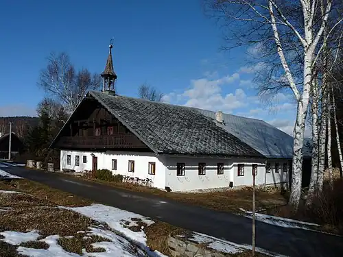 Obrázek ukazuje dům volarského typu v obci Dobrá ve stavu v roce 2014. Přízemí je bíle omítnuto, patro má typickou pavlač s ozdobným zábradlím. Střecha má charakteristický tvar stanové střechy s malým sklonem, je ale již kryta moderní krytinou (eternit). Na hřebeni střechy v průčelí se nachází další charakteristický prvek šumavské venkovské architektury: malá věžička se zvonem.