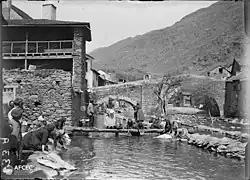 Ženy perou prádlo u hráze mlýna a v pozadí je most, ve vesnici Esterri d'Àneu