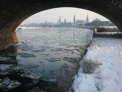 Barevná fotografie s průhledem pod klenbou mostu na zasněžený břeh a částečně zamrzlou hladinu Labe