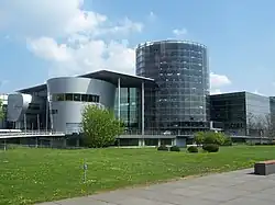 Barevná fotografie s pohledem na komplex moderních budov shromážděných kolem domu ve tvaru tubusu