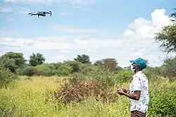 Místní pracovník ovládající dron, v pozadí savana zarostlá křovinami