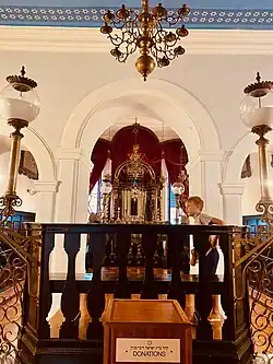 Interiér dubrovnické synagogy, detail s dřevěnou bimou uprostřed a kasičkou na cedaku. Srpen 2024.