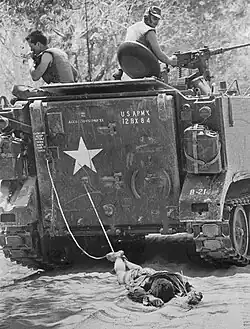 „Tan Binh, Jižní Vietnam: Tělo vojáka Vietkongu, zabitého během zuřivých nočních bojů, je vlečeno za americkým obrněným transportérem; 24. února 1966; zatímco spojenecké jednotky počítaly mrtvé ponechané na bojišti 35 mil severozápadně od Saigonu. Tvrdé jádro jednotek Vietkongu zaútočilo na americké a australské pozice během 'Operace Rolling Stone'.“ Tato fotografie získala ocenění World Press Photo of the Year za rok 1966.