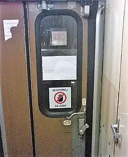 Dveře s otočnou klikou a cedulí Neotvírej za jízdy, focené z uličky vlaku