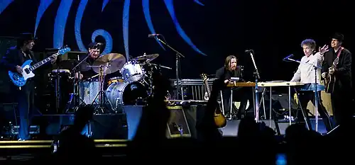 Dylan together with five members of his band onstage. Dylan, dressed in a white shirt and black pants, is second from right.