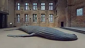 Socha mrtvého keporkaka ze zřetelně sploštělým tělem na zemi v budově připomínající továrnu