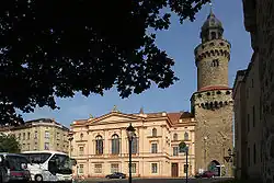 Barevná fotografie s pohledem na masivní gotickou obrannou věž a historizující budovu přírodovědeckého muzea