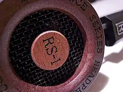 Mušle sluchátek z mahagonu červenohnědé barvy a se štítkem s názvem modelu.