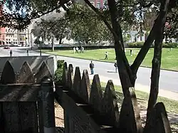 Pohled na Dealey Plaza skrze dřevěnou palisádu na travnatém pahorku (grassy knoll) – zde měl být ukrytý druhý střelec