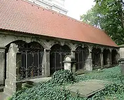 Barevná fotografie zachycující ubíhající sedlovou střechu, pod níž jsou zamřížované portály s hrobkami