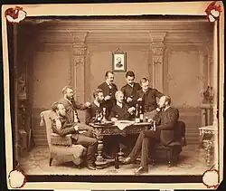 Skupina mužů, kteří kouří dýmku a pijí portské víno, Zleva: 1. Jacob Halvorsen, student 2. Fredrik Finckenhagen 3. Oluf E. Larsen, 4. Hans Ramm, pozdější ředitel školy v Namsos 5. Gustaf Amneus 6. student medicíny Jon Melhus, později lékař v Nord-Trøndelag 7. neznámý 8. Otto Winther, ředitel pobočky Savings Bank v Oslo.