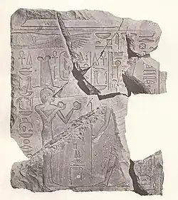 Velmi poškozené fragmenty vápencového překladu u dveří, na kterých proti sobě stojí dvě osoby, osoba nalevo má korunu, šaty a v rukou drží dvě koule. Druhé osobě jsou vidět jen nohy a jedna ruka. Kolem osob se nachází symboly a hieroglyfy.