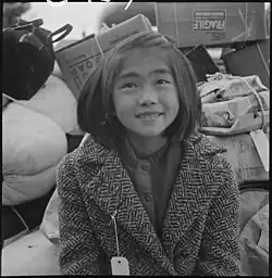 Mladá členka evakuované rodiny čeká na evakuační autobus. Evakuované osoby japonského původu jsou umístěni do internačních táborů, Hayward, Kalifornie, 8. května 1942.